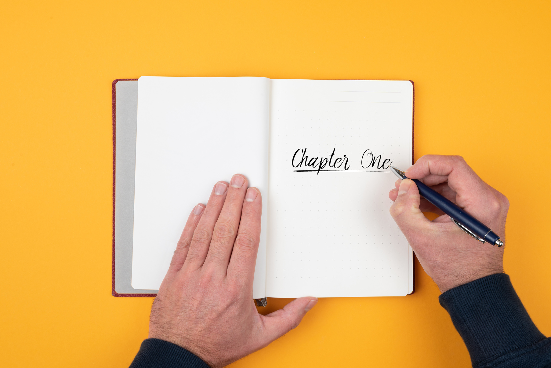 Top View of Person Writing Words CHAPTER ONE on Notebook